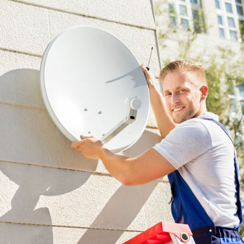 Young Man Fitting TV Satellite Dish To Wall